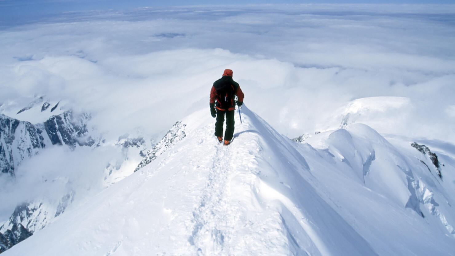 Climber on steep summit of mountain in snow.