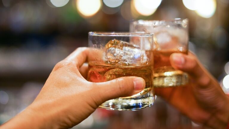 two men clinking glasses of whiskey drink alcohol beverage together at counter in the pub