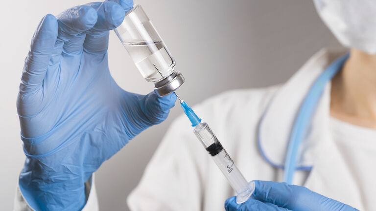 A doctor in a white coat and protective gloves holds a medicine in a syringe or a covid-19 Vaccine. The hand of the medical worker knocks on the syringe and knocks out the air with his finger. The concept of health care, vaccination, treatment of diseases