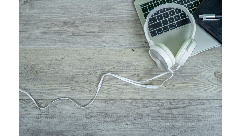 White headphones with computer laptop on wooden office desk for entertainment and leisure online concept.