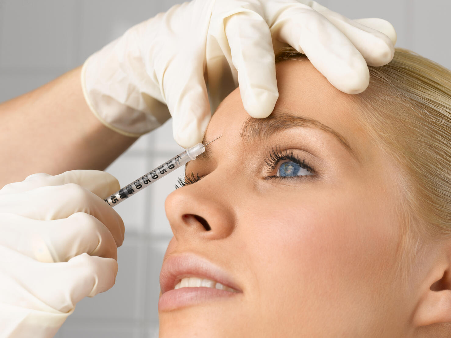 Person injecting young woman's forehead with small syringe, close up, side view, studio shot