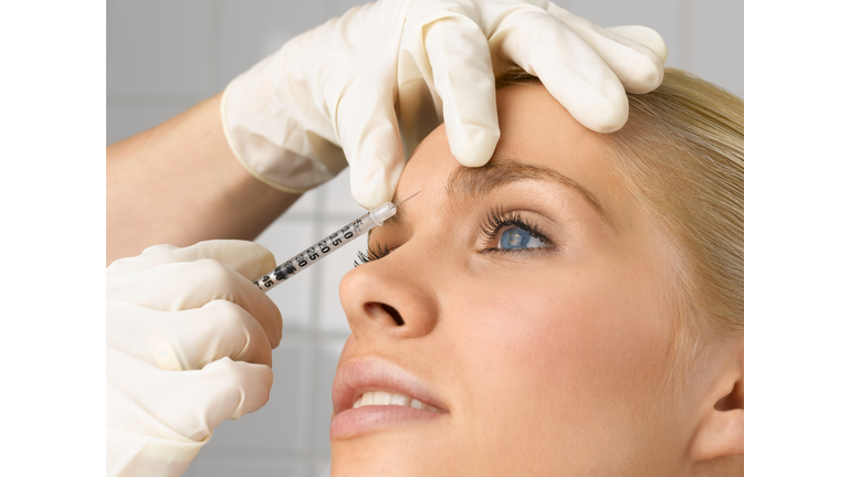 Person injecting young woman's forehead with small syringe, close up, side view, studio shot