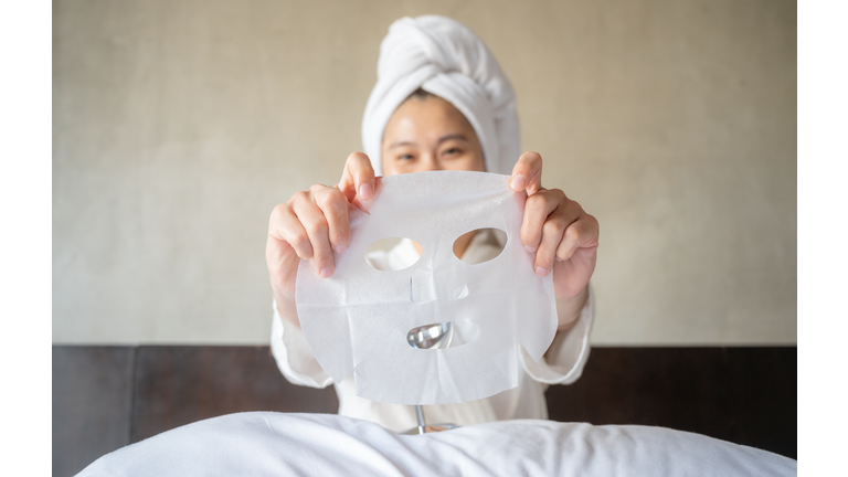 Smiling Asian woman holding a facial mask before applying to her face.