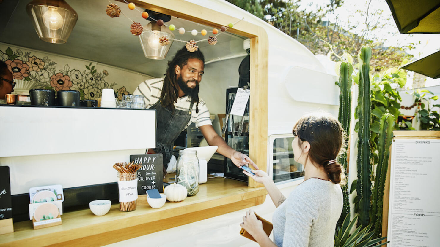 Smiling food truck owner taking credit card for payment from customer