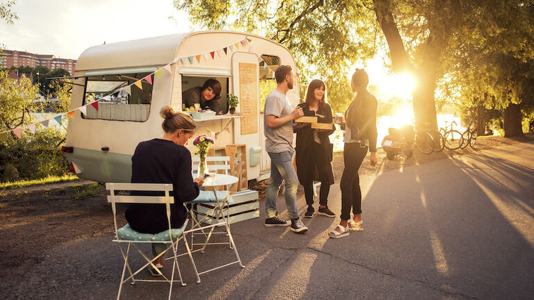 Owner looking at customers standing on street through food truck window