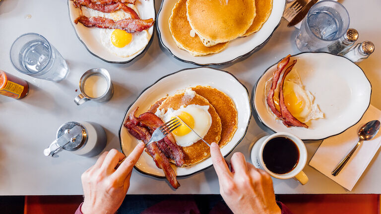 Man eating pancakes with bacon and eggs in a traditional American diner, personal perspective overhead view