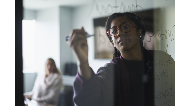 Businesswoman writing on glass wall during meeting