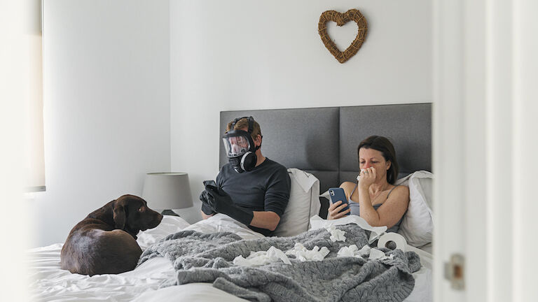 Couple in bed. Wife has the flu. Husband isn't taking any risks..!