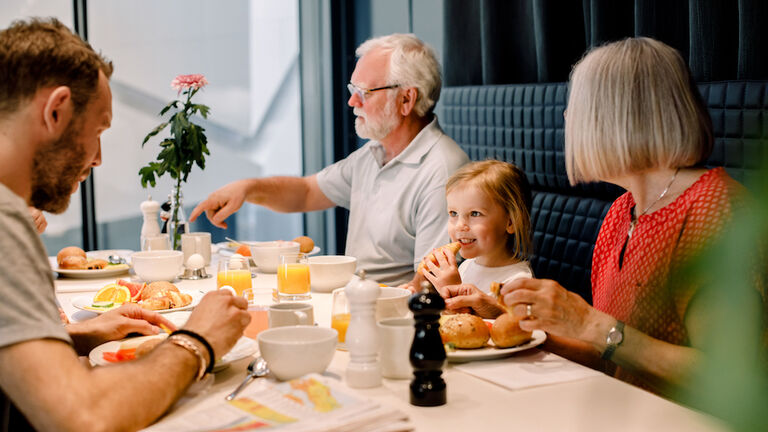 Smiling girl looking at father while having food with grandparents at restaurant