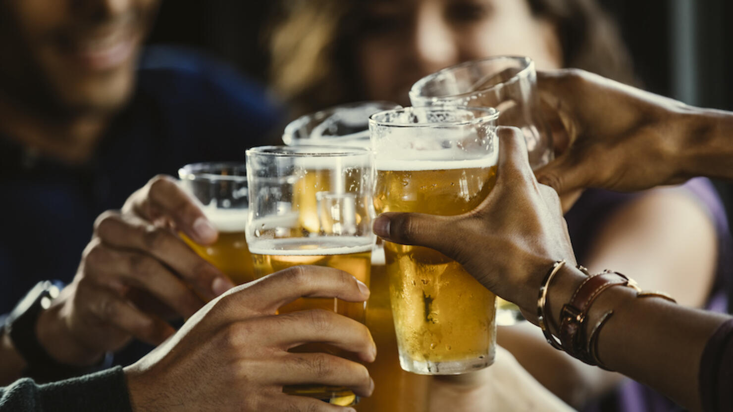 Group of friends toasting beer glasses at table in bar