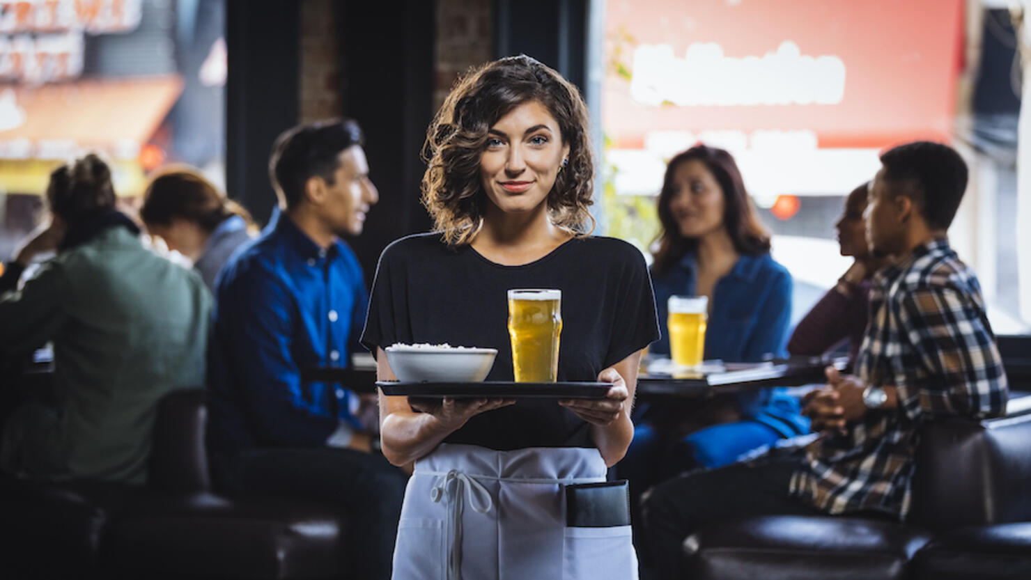 Portrait of smiling waitress carrying food and drink on serving tray in bar