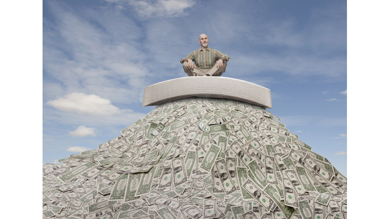 Caucasian businessman sitting on mattress on mountain of money