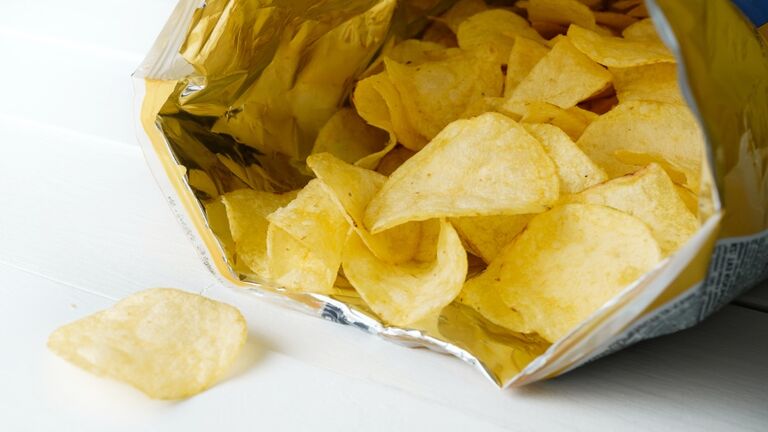 Crispy Fried Greasy Potato Chips fall out or are spilled out of the package, on a white background or table. The concept of unhealthy diet and lifestyle, accumulation of excess weight.