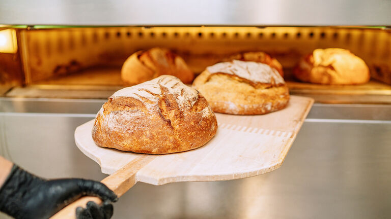 Baker putting bread in the bakery oven cowering on the floor of the bakery
