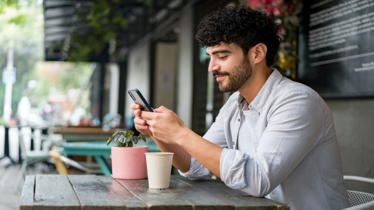 Happy man drinking checking his cell phone at a coffee shop while drinking a cappuccino