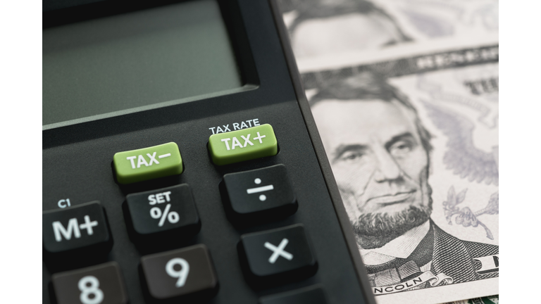 Closed up shot of TAX minus / plus buttons with text TAX RATE on calculator with background of US Dollar banknotes, United States government tax calculation