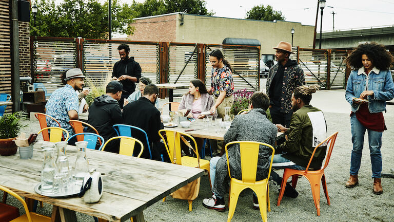 Group of friends hanging out at table at outdoor restaurant sharing drinks and food