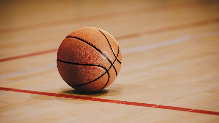 Classic Basketball on Wooden Court Floor Close Up with Blurred Arena in Background. Orange Ball on a Hardwood Basketball Court