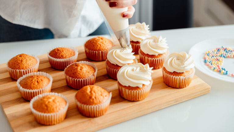 Woman decorates freshly baked cupcakes with cream