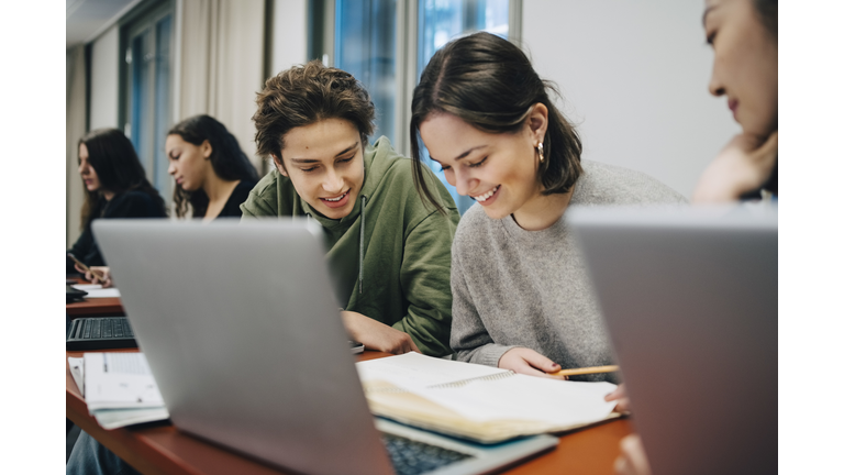 Smiling teenage students studying at desk in school