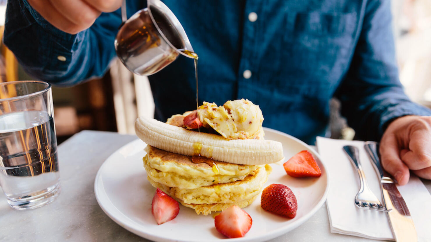 Man pouring maple syrup on pancakes with banana and strawberry