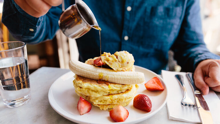 Man pouring maple syrup on pancakes with banana and strawberry