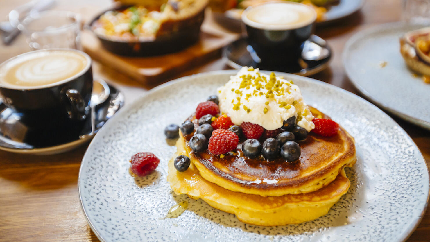 Stack of pancakes with fresh blueberry, raspberry and ricotta cheese on a plate, served with coffee in cafe