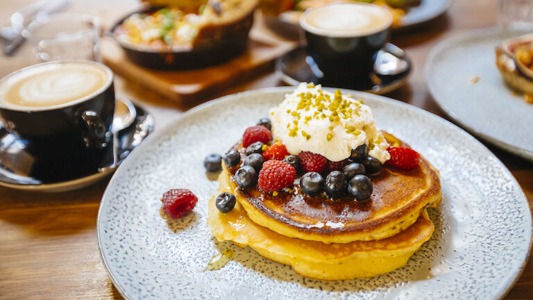 Stack of pancakes with fresh blueberry, raspberry and ricotta cheese on a plate, served with coffee in cafe