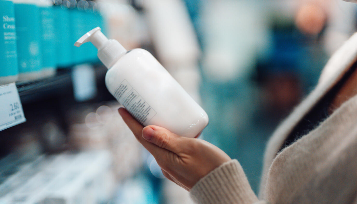 Close-up Shot Of Female Hand Holding Hand Cream Bottle In Supermarket
