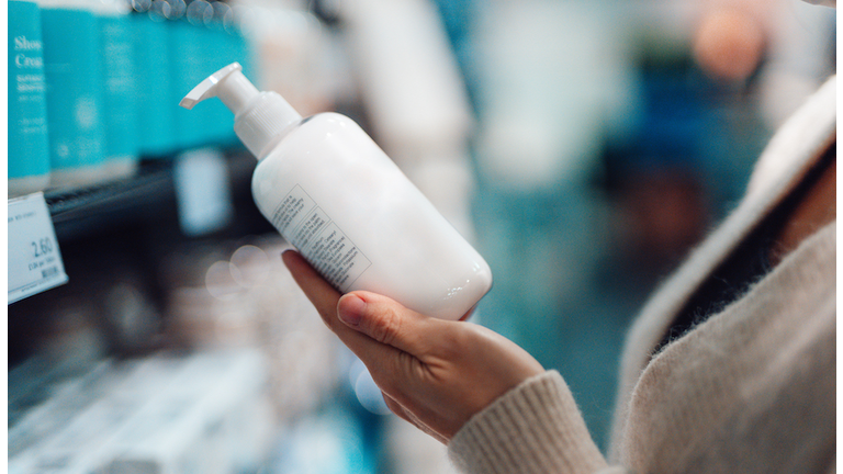 Close-up Shot Of Female Hand Holding Hand Cream Bottle In Supermarket