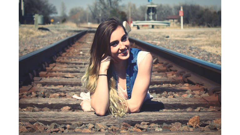 Portrait Of Smiling Young Woman Lying On Railroad Track