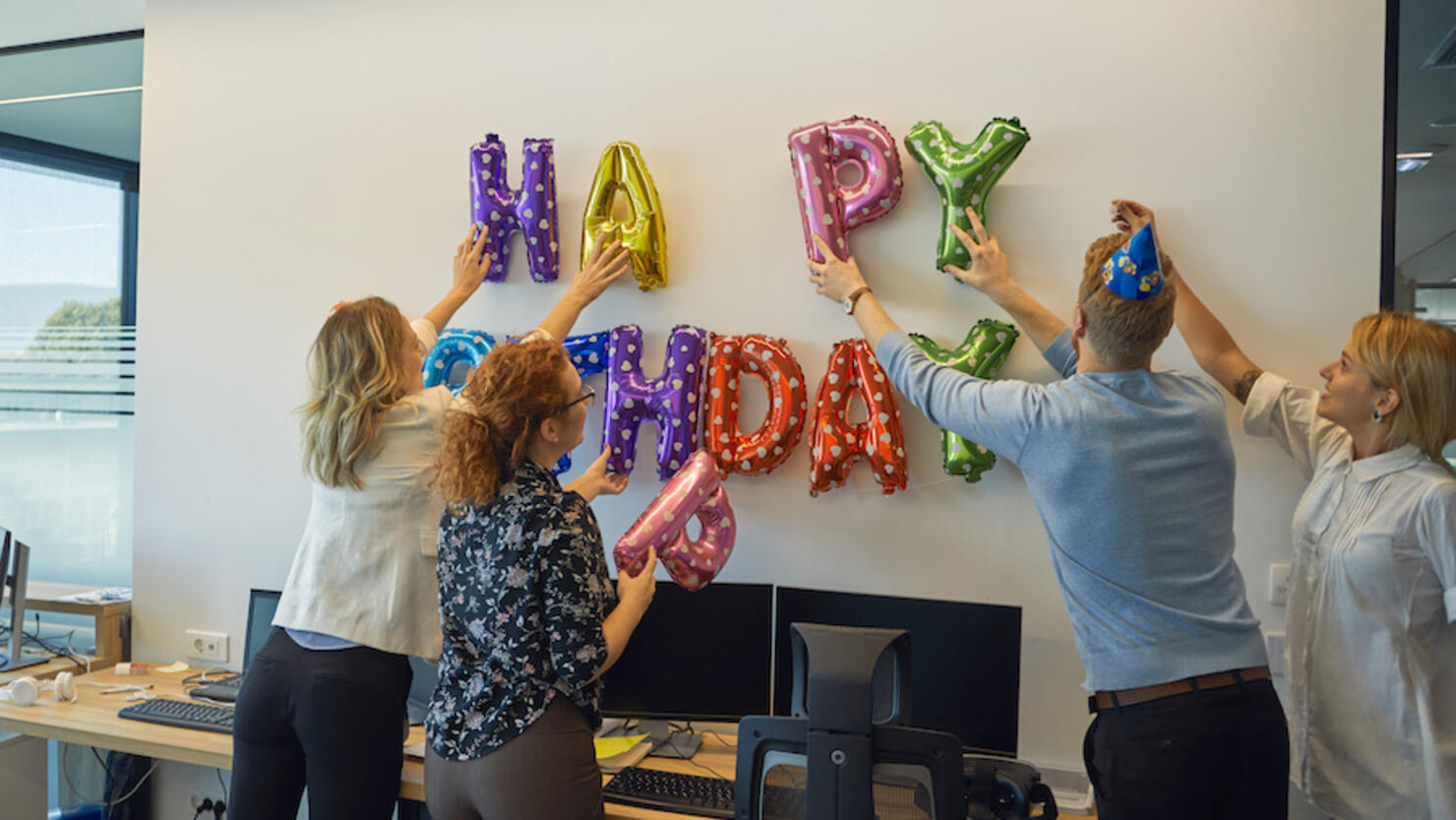 Colleagues decorating office with happy birthday writing