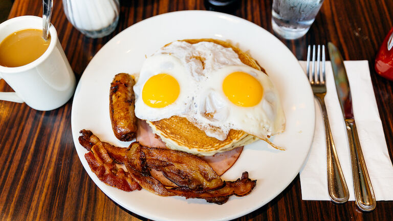 Traditional American breakfast with pancakes, fried eggs, bacon, sausage and ham served in a diner