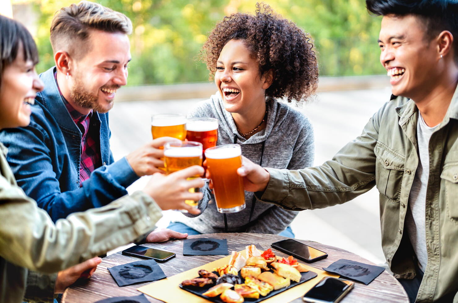 Young multicultural friends drinking and toasting beer at brewery bar patio - Youth life style concept with men and women having fun together out side - Bright vivid filter with focus on mid girl