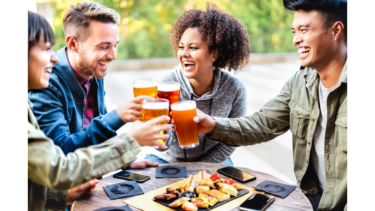 Young multicultural friends drinking and toasting beer at brewery bar patio - Youth life style concept with men and women having fun together out side - Bright vivid filter with focus on mid girl
