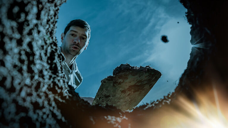 Surprised man digger finding glowing treasures in the dirty ground on a dark moonlit night