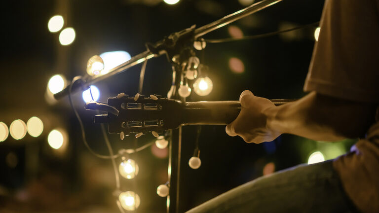 Rear view of the man sitting play acoustic guitar on the outdoor concert with a microphone stand in the front, musical concept.