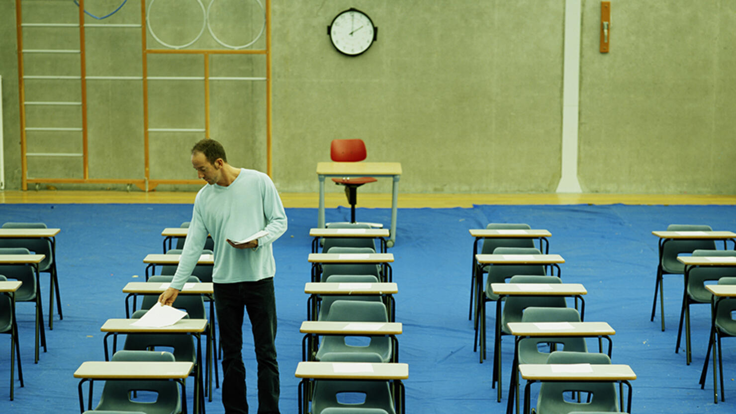 Male teacher setting out papers in empty exam hall