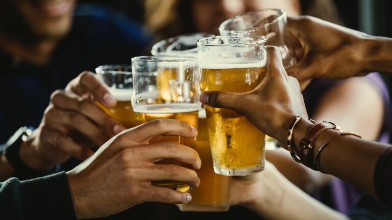 Group of friends toasting beer glasses at table in bar