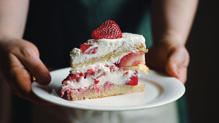 Woman in apron holding slice of strawberry cake