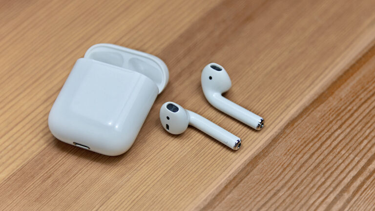 Mobile airpods on wooden blurred background. Apple wireless earphones with charger box, chosen focus.