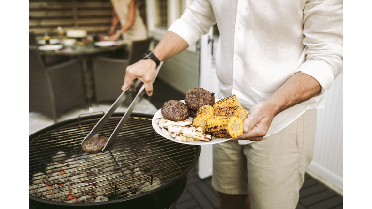 Midsection of mature man preparing barbecue meal in back yard