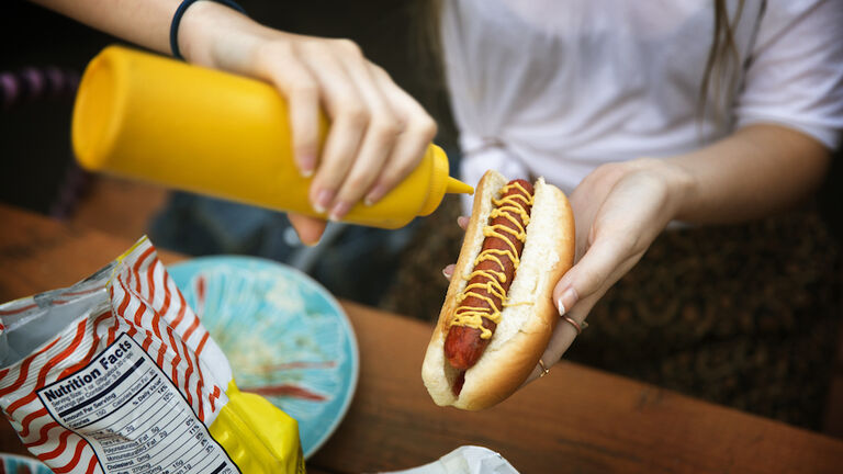 Cropped image of woman pouring mustard sauce on hot dog at garden party
