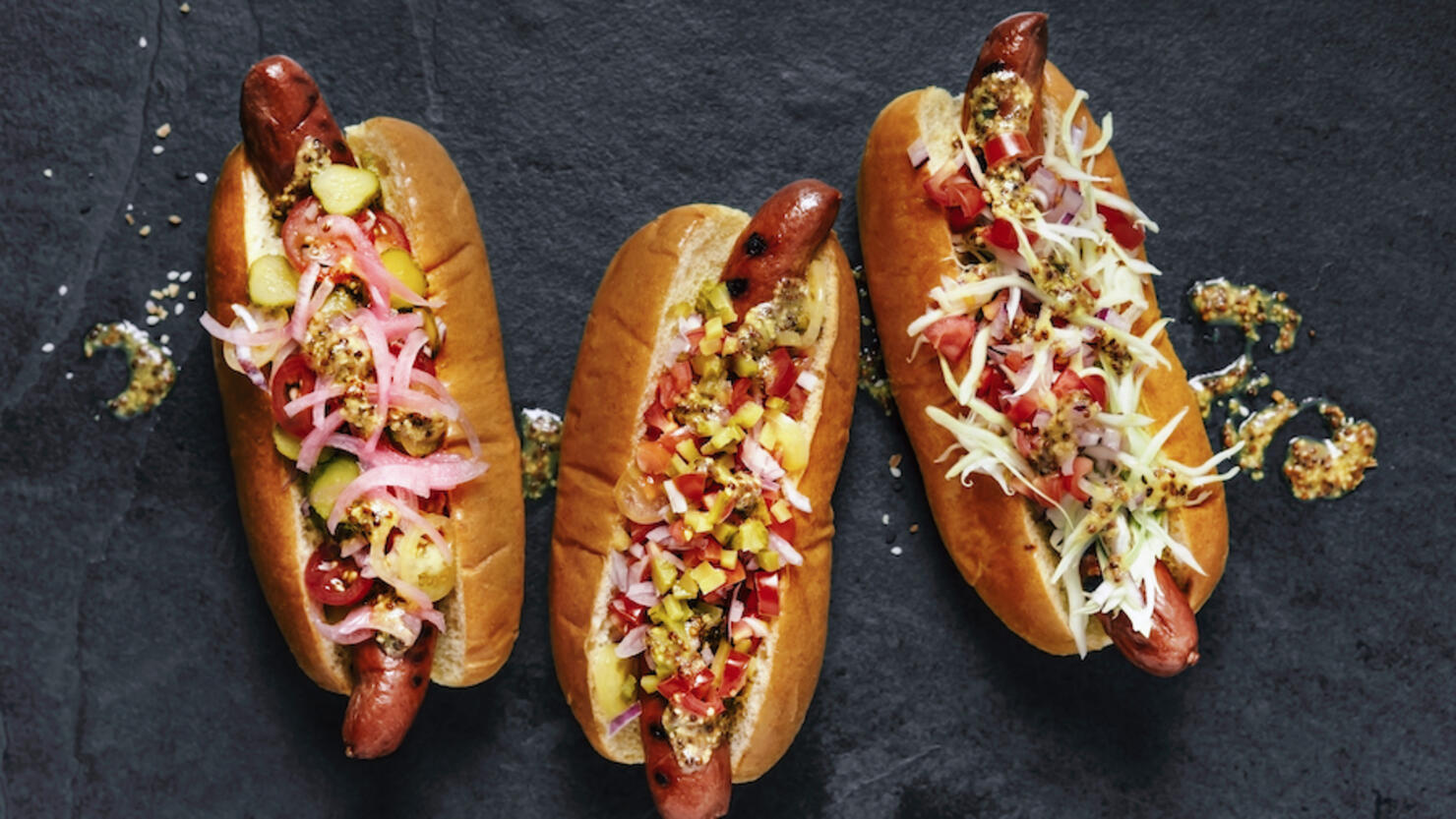 Three gourmet hot dogs on black background
