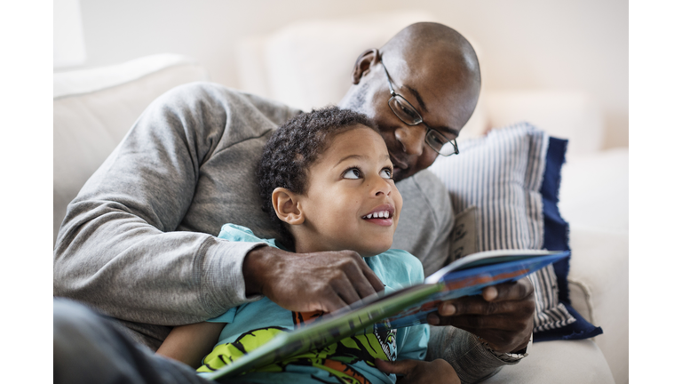 Smiling boy looking at father while reading picture book at home