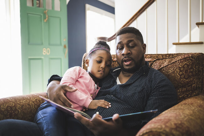 Father and daughter reading book in living room at home