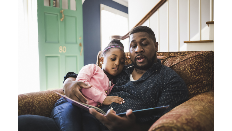 Father and daughter reading book in living room at home