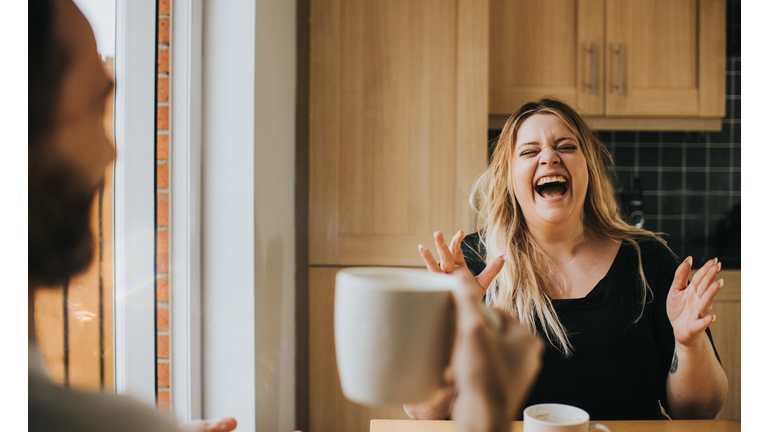 Man and Woman drink coffee / tea together as woman laughs hysterically