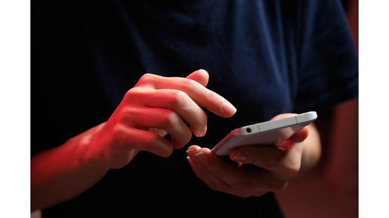 A mobile phone in the hands of a girl. A young woman in a black T-shirt is holding a phone. The fraudster sends an email message. The work of a freelancer, businessman. The wife checks messages and notifications on social networks. Wireless technologies.