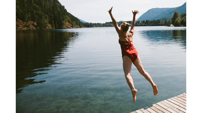 Caucasian woman jumping from dock into rural lake